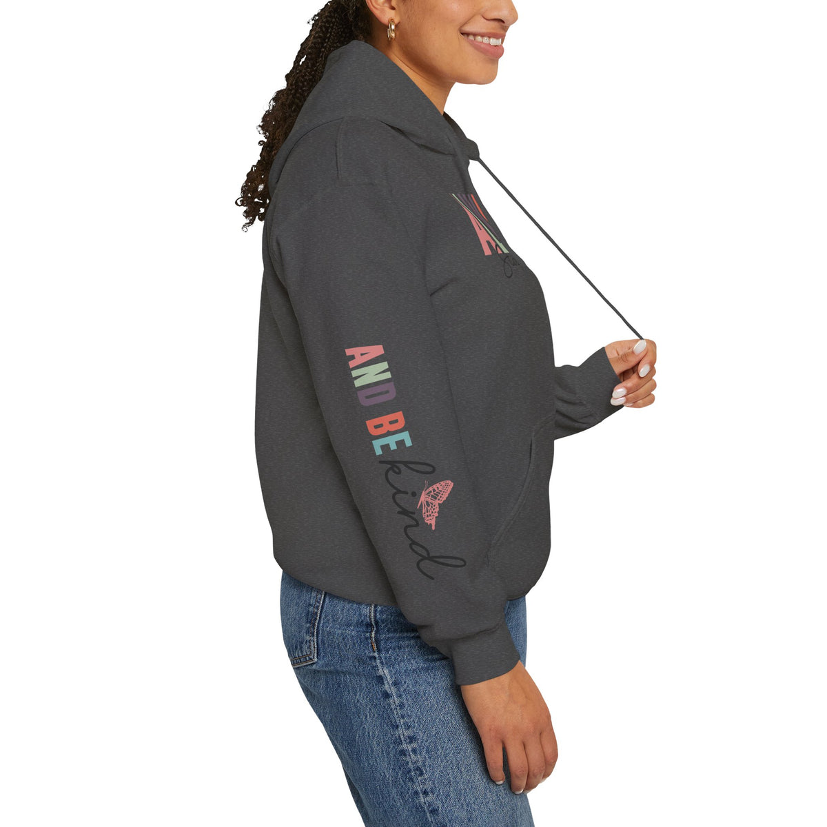 A person wearing a dark gray hoodie with text graphics on the sleeve 'ALWAYS BE KIND', paired with blue jeans, shown from a side profile against a white background.