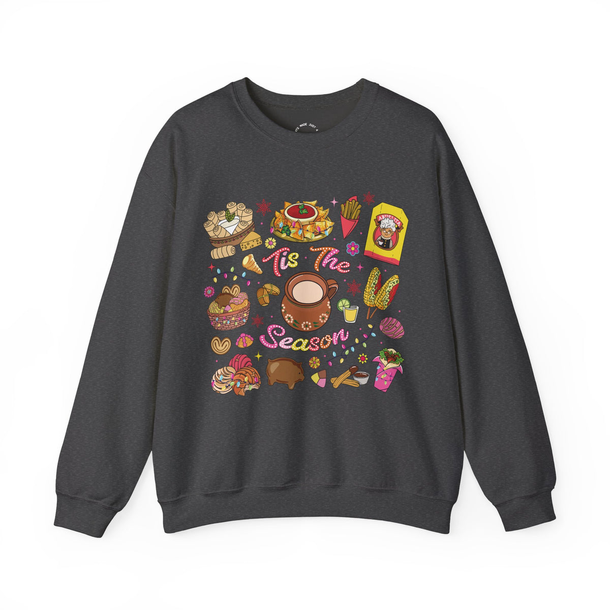 A dark gray crewneck sweatshirt featuring a colorful Christmas-themed graphic print with illustrations of seasonal hispanic treats and the text 'Tis The Season'.