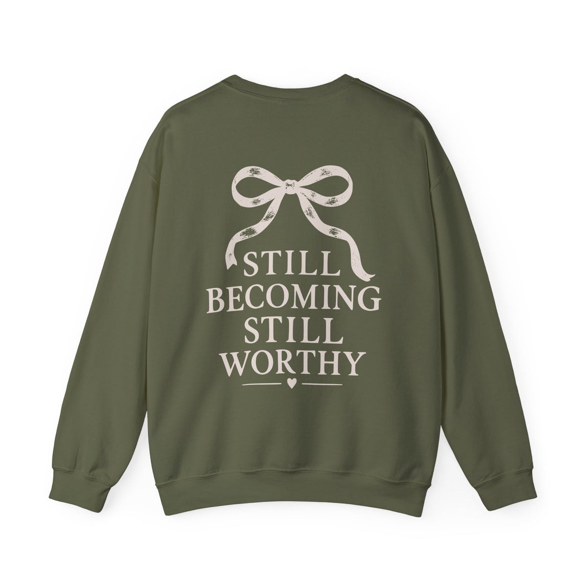 An olive green crewneck sweatshirt shown from the back, featuring a cream graphic of a ribbon bow and the text 'STILL BECOMING STILL WORTHY' printed on the back.