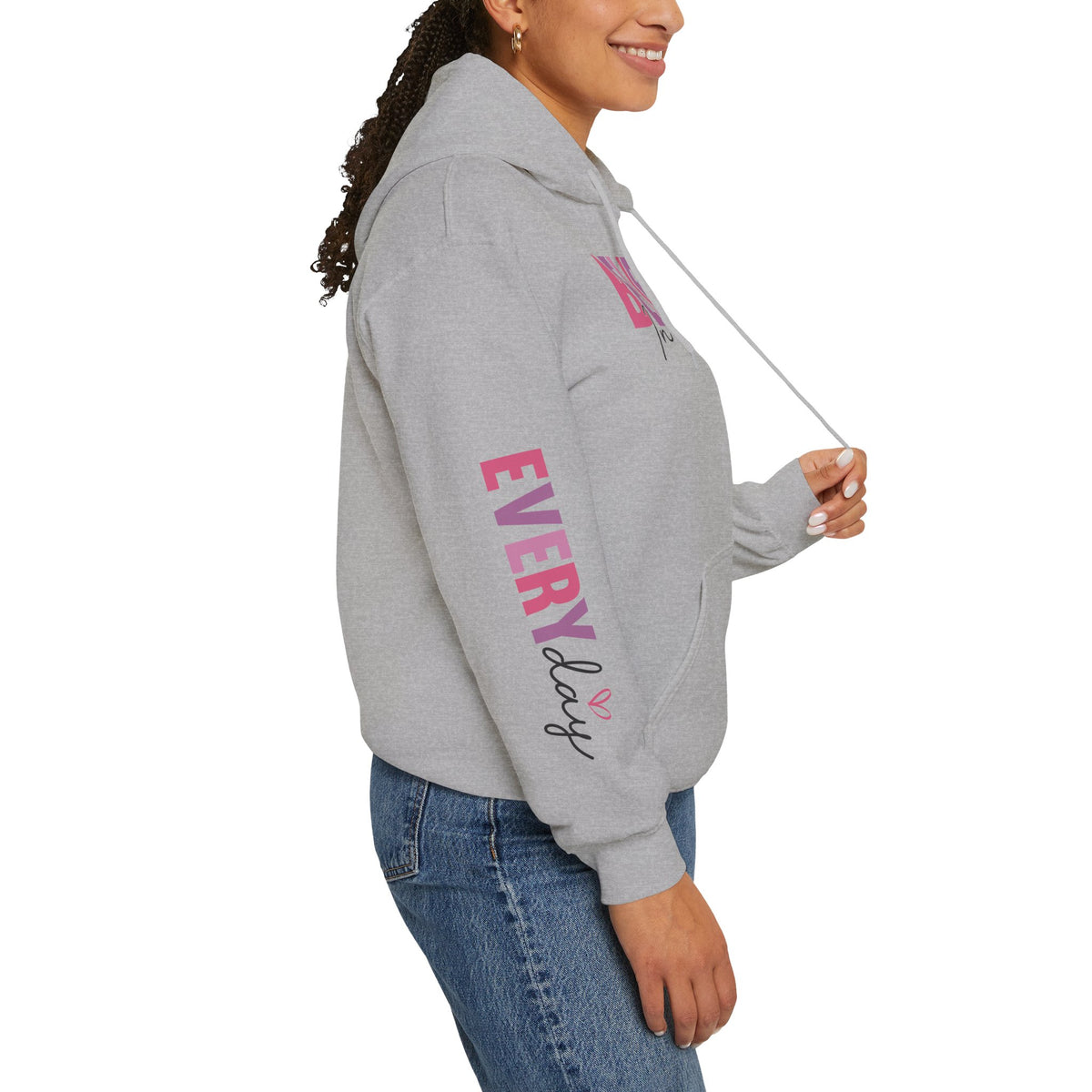 A woman wearing  gray hoodie with pink and purple text graphics on the sleeve 'EVERY DAY', paired with blue jeans, shown from a side profile against a white background.