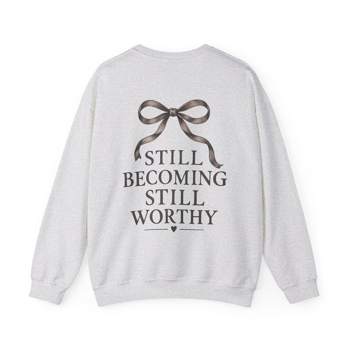 A light heather gray sweatshirt shown from the back, featuring a dark brown ribbon graphic above the text 'STILL BECOMING STILL WORTHY'.