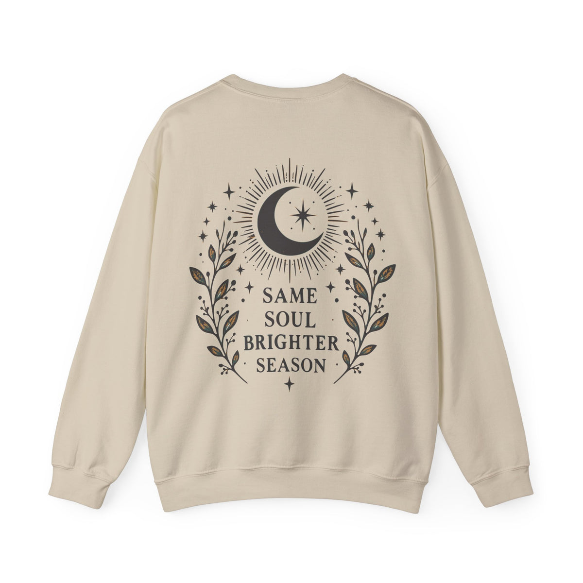 A beige crewneck sweatshirt shown from the back, featuring a dark brown graphic of a crescent moon, stars, and leafy branches with the text 'SAME SOUL BRIGHTER SEASON'.