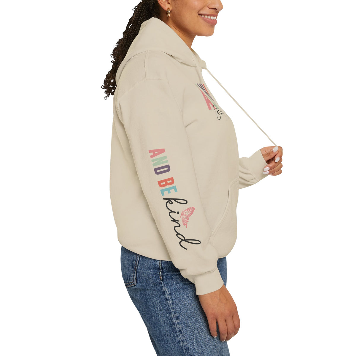 A woman wearing a beige hoodie with text graphics on the sleeve 'ALWAYS BE KIND', paired with blue jeans, shown from a side profile against a white background.