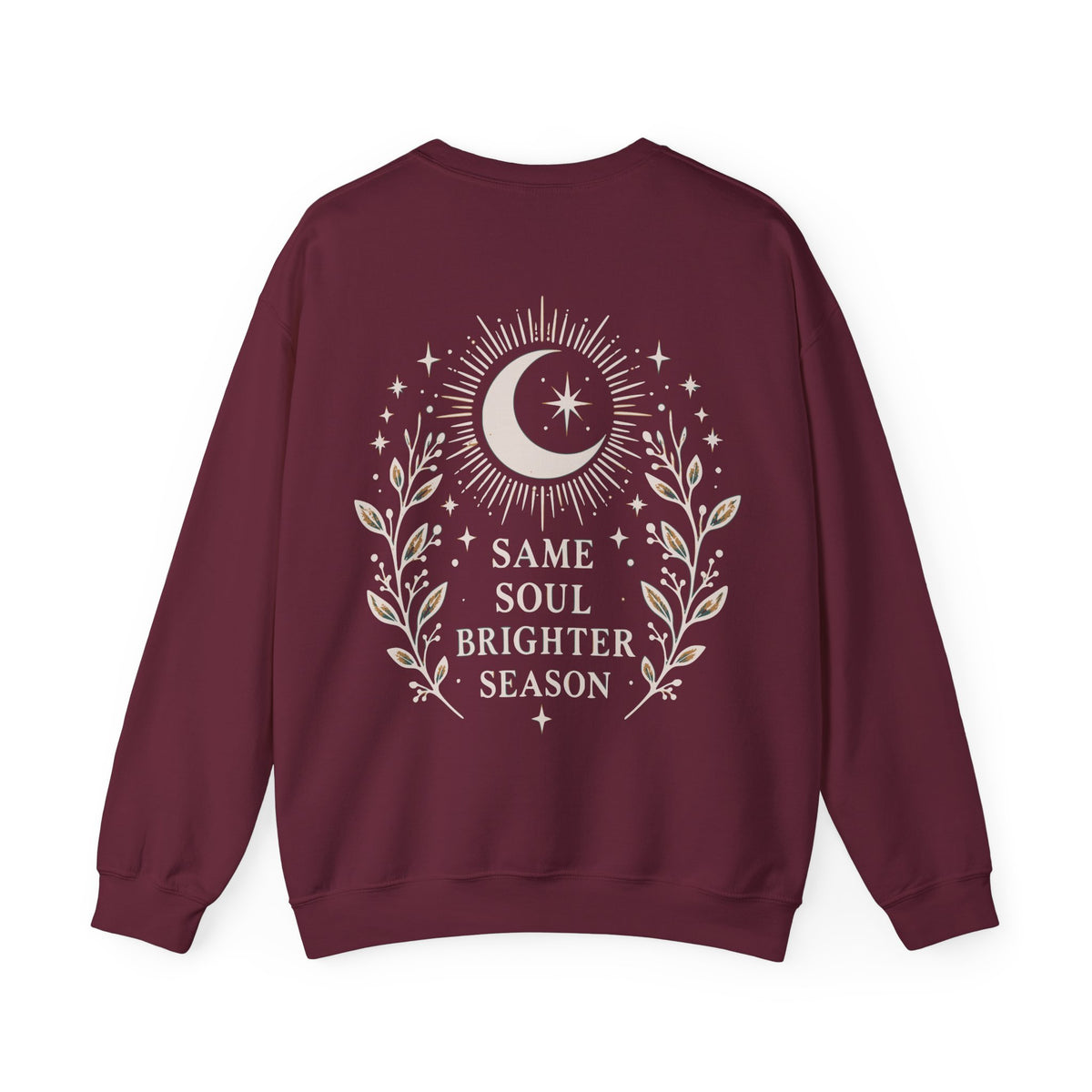A maroon crewneck sweatshirt with a cream-colored celestial graphic on the back, featuring a crescent moon, stars, and the text 'SAME SOUL BRIGHTER SEASON' framed by leafy branches.