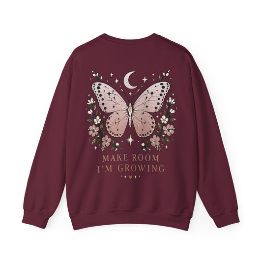 A maroon crewneck sweatshirt shown from the back, featuring a graphic of a pink butterfly surrounded by flowers, a crescent moon, and stars, with the text 'MAKE ROOM I'M GROWING' printed below.