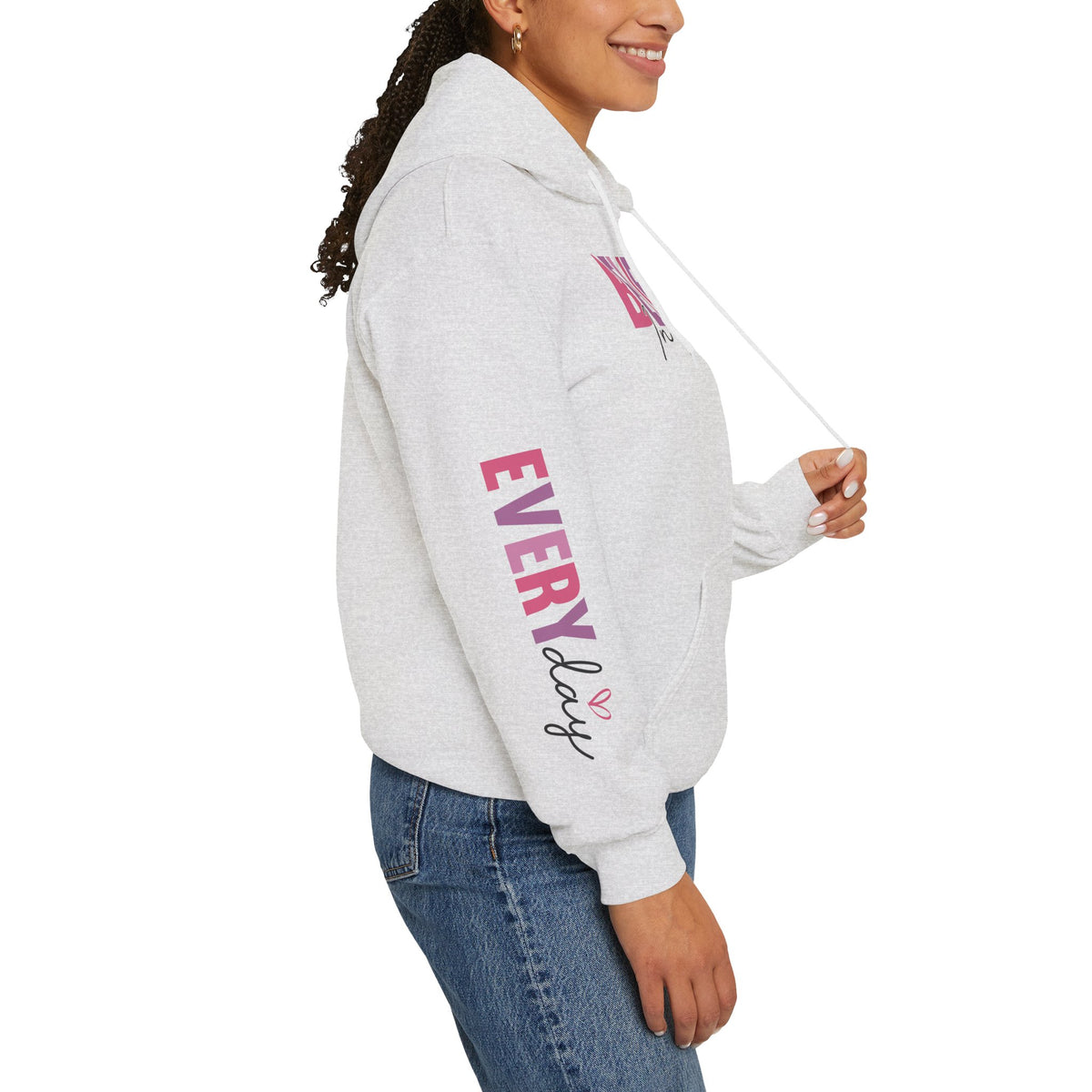 A woman wearing a light heather gray hoodie with pink and purple graphics on the sleeve, paired with blue jeans, shown from a side profile against a white background.
