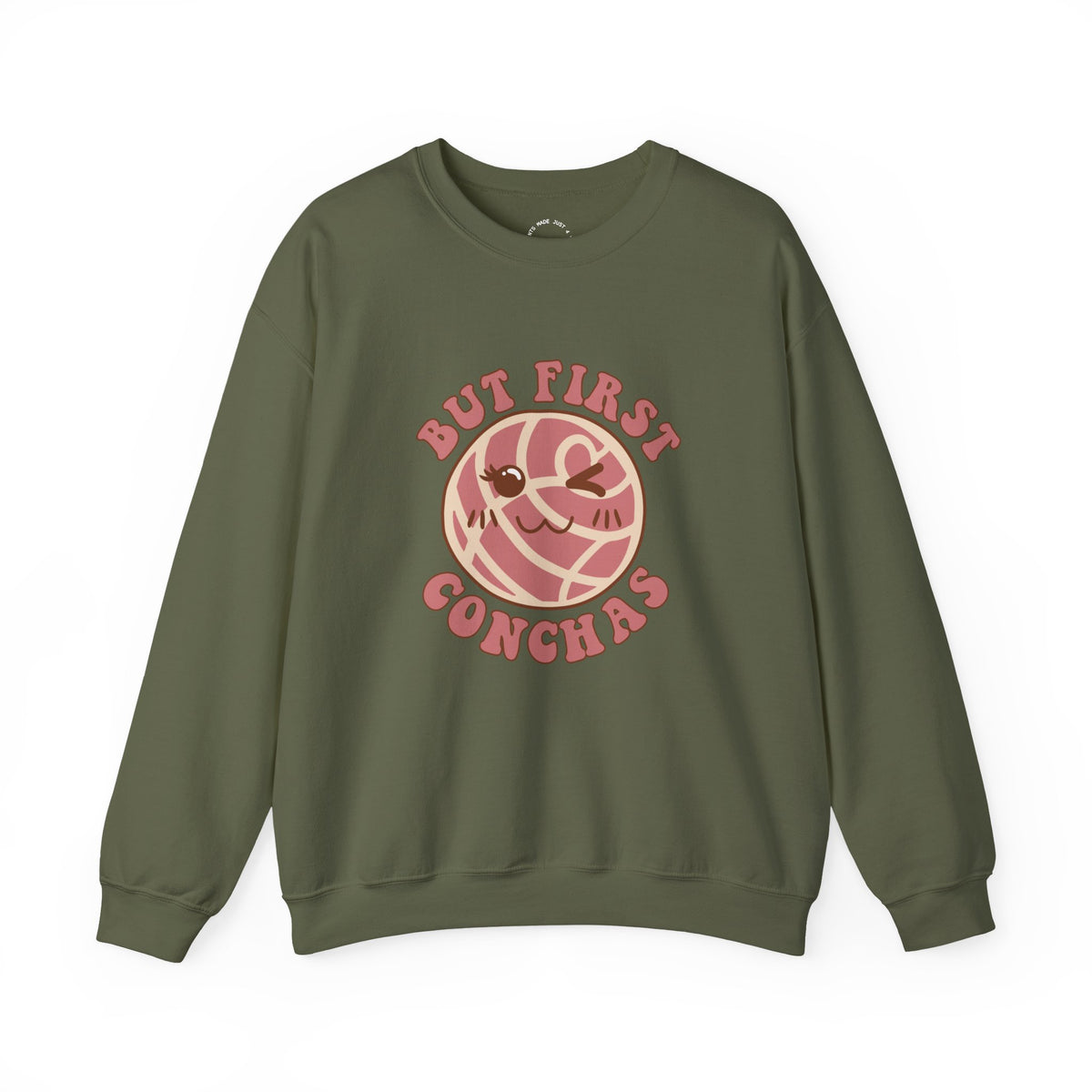 A military green crewneck sweatshirt featuring a graphic of a winking concha with the text 'BUT FIRST CONCHAS' in pinkish-red lettering.