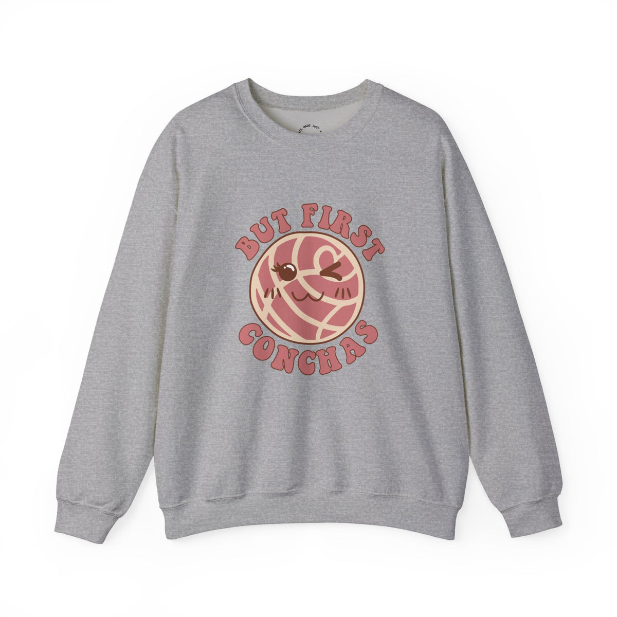 A heather gray crewneck sweatshirt featuring a graphic of a winking concha with the text 'BUT FIRST CONCHAS' in pinkish-red lettering.