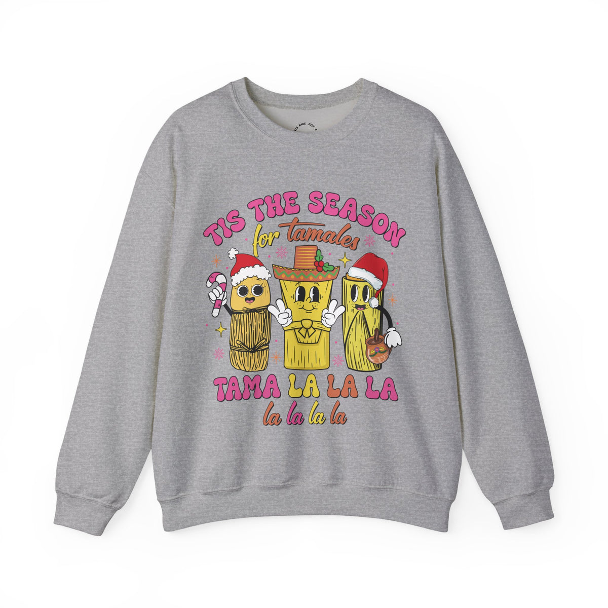 A heather gray crewneck sweatshirt featuring a colorful graphic of three tamale characters wearing Santa hats and a sombrero, with the text 'TIS THE SEASON for Tamales' and 'TAMA LA LA LA la la la la'.