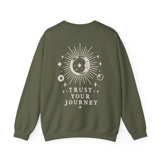 An olive green crewneck sweatshirt with a cream celestial graphic on the back featuring a sun, moon, stars, and the text 'TRUST YOUR JOURNEY'.