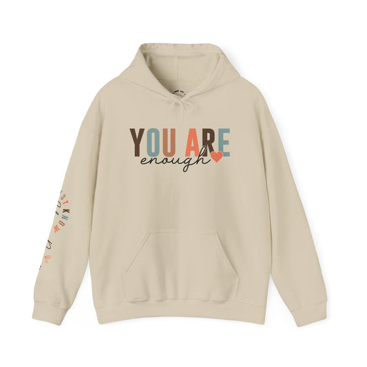 A beige pullover hoodie with a front kangaroo pocket and a graphic text print reading 'YOU ARE enough' on the chest with a small heart and 'Just Know Your Power' on the sleeve, shown on a plain white background.