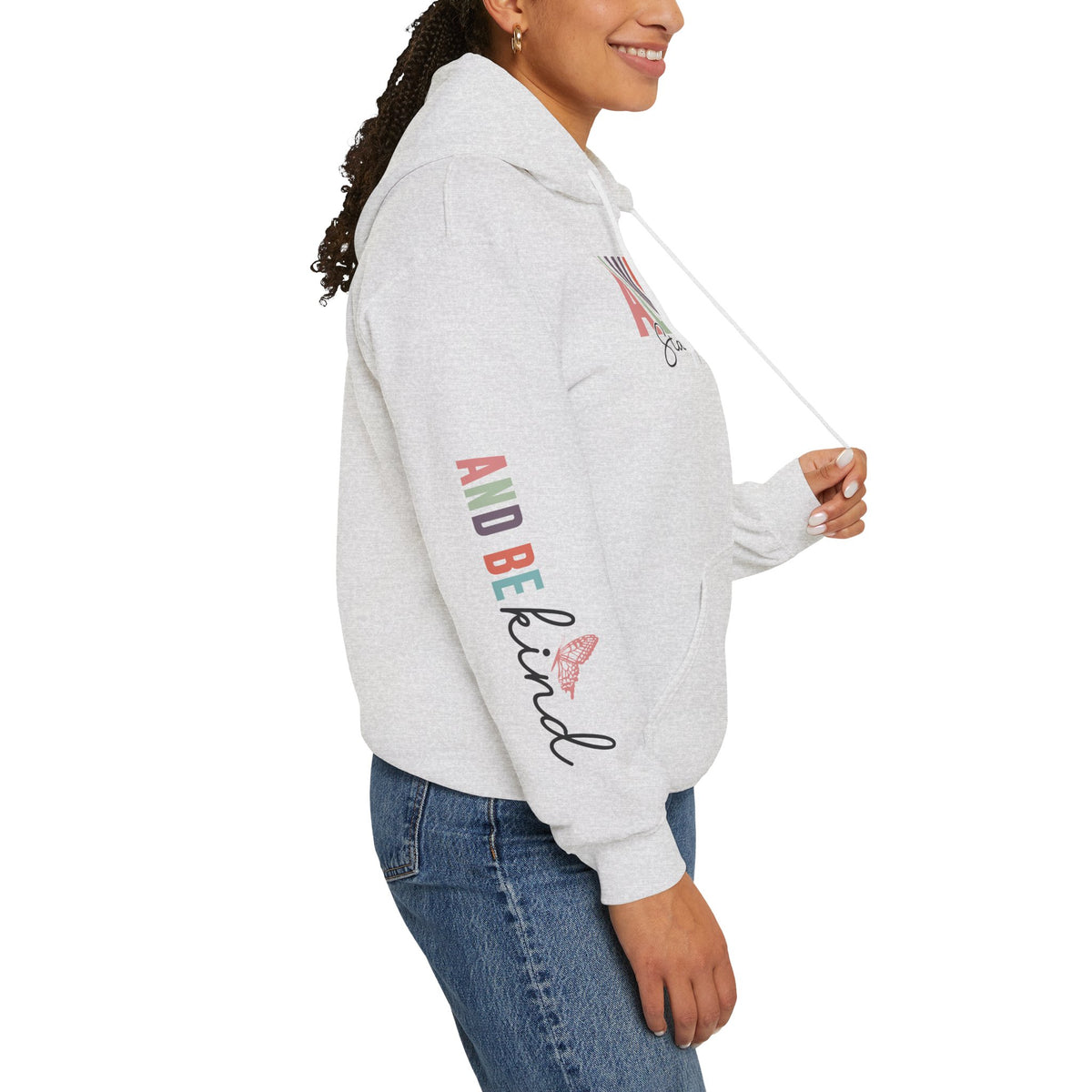 A woman wearing a light heather gray hoodie with text graphics on the sleeve 'ALWAYS BE KIND', paired with blue jeans, shown from a side profile against a white background.