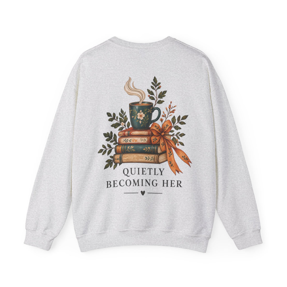 A light heather gray crewneck sweatshirt shown from the back, featuring a graphic print of a steaming mug on a stack of books with a ribbon, surrounded by leaves, and the text 'QUIETLY BECOMING HER'.