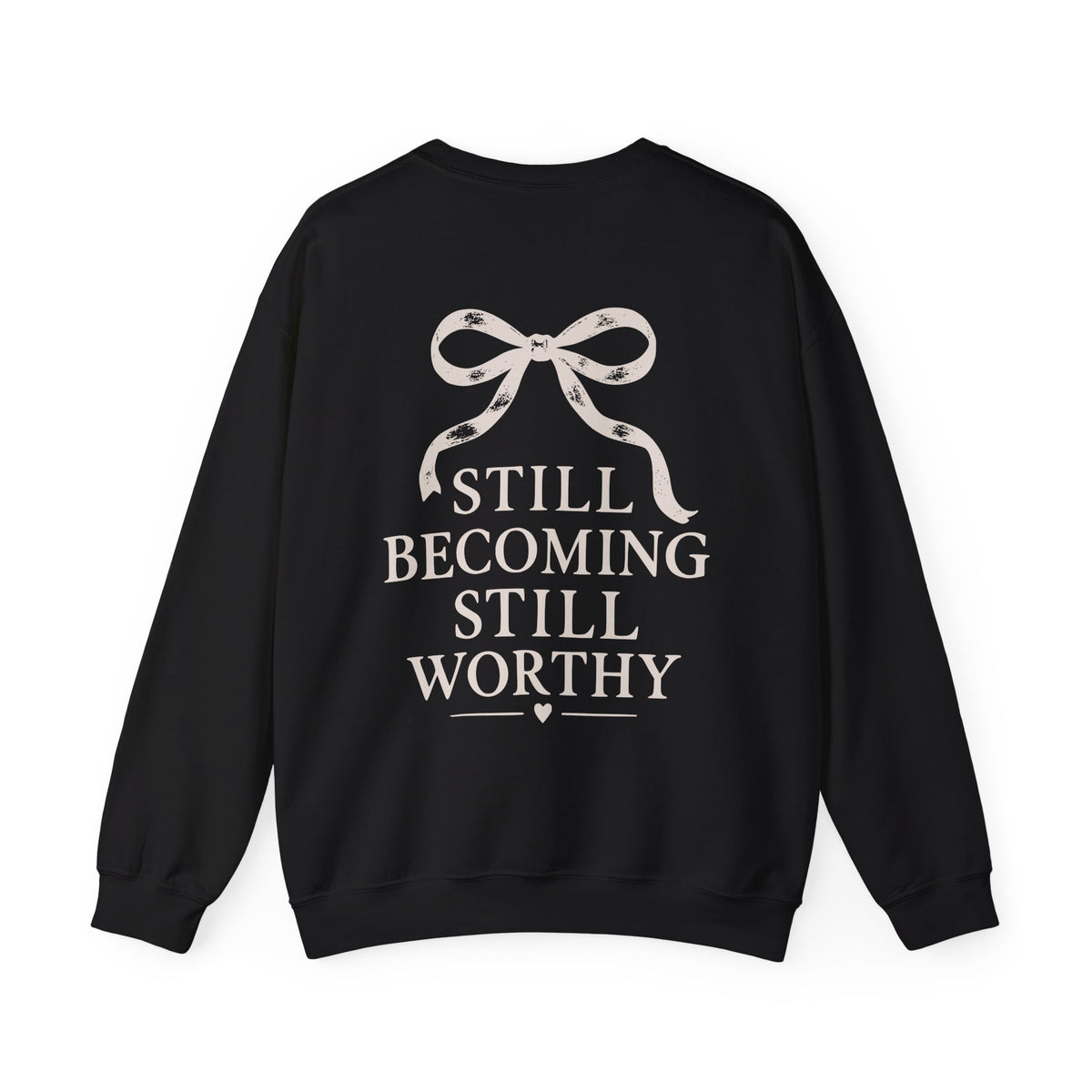 A black crewneck sweatshirt with a graphic on the back featuring a ribbon bow and the text 'STILL BECOMING STILL WORTHY' in a light beige color, shown against a plain white background.