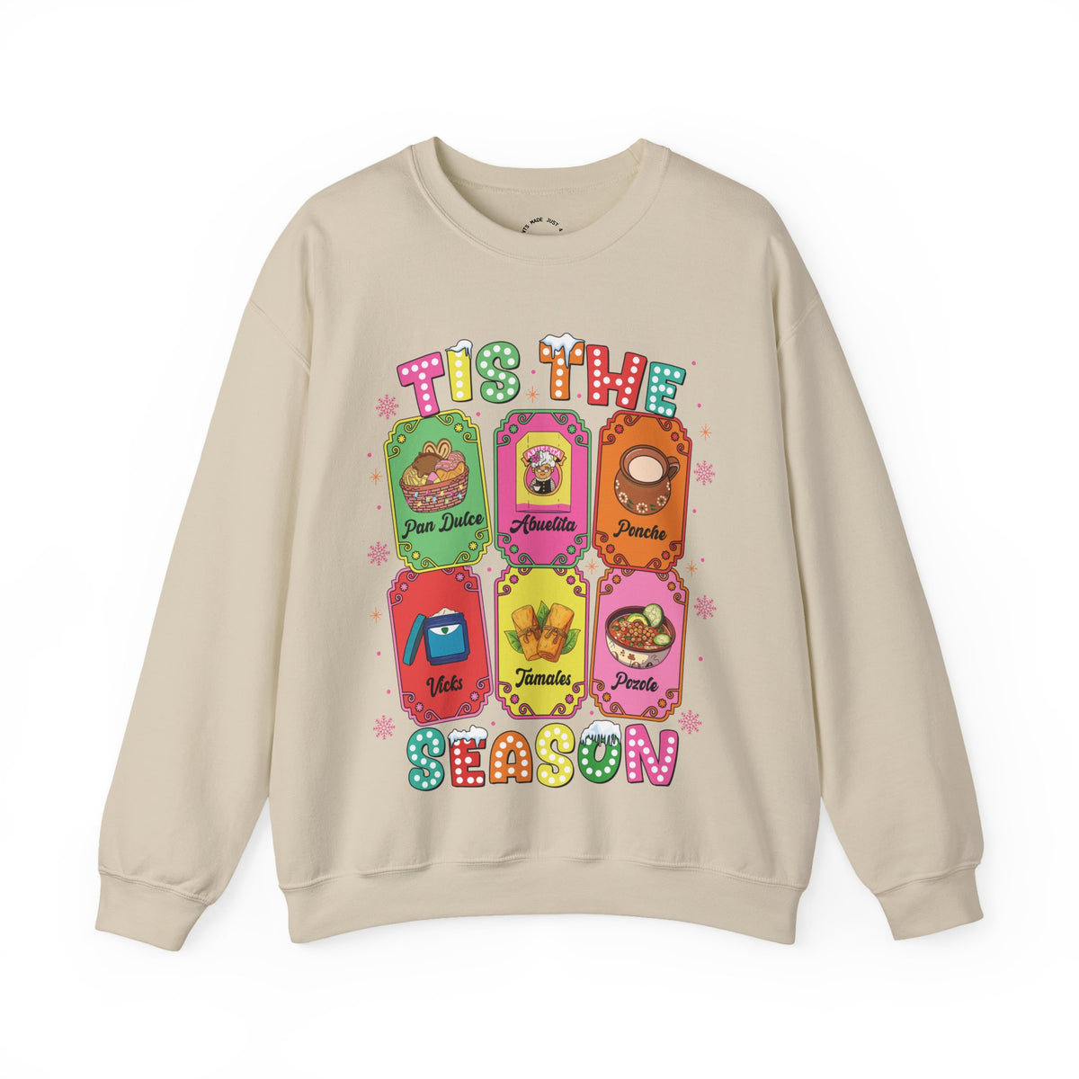 A beige crewneck sweatshirt featuring a colorful graphic print of six Christmas-themed ticket illustrations with Latino traditions with the text 'TIS THE SEASON' in a retro, bubbly font.