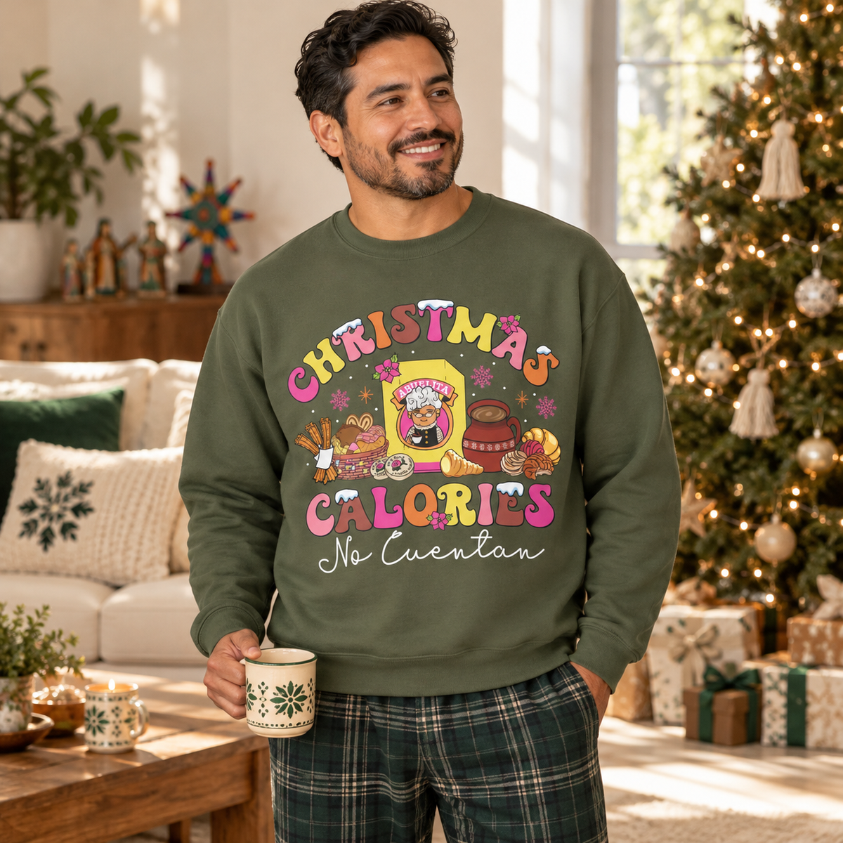 A man wearing an olive green crewneck sweatshirt with a colorful 'Christmas Calories No Cuentan' graphic, standing in a cozy living room with a Christmas tree in the background.