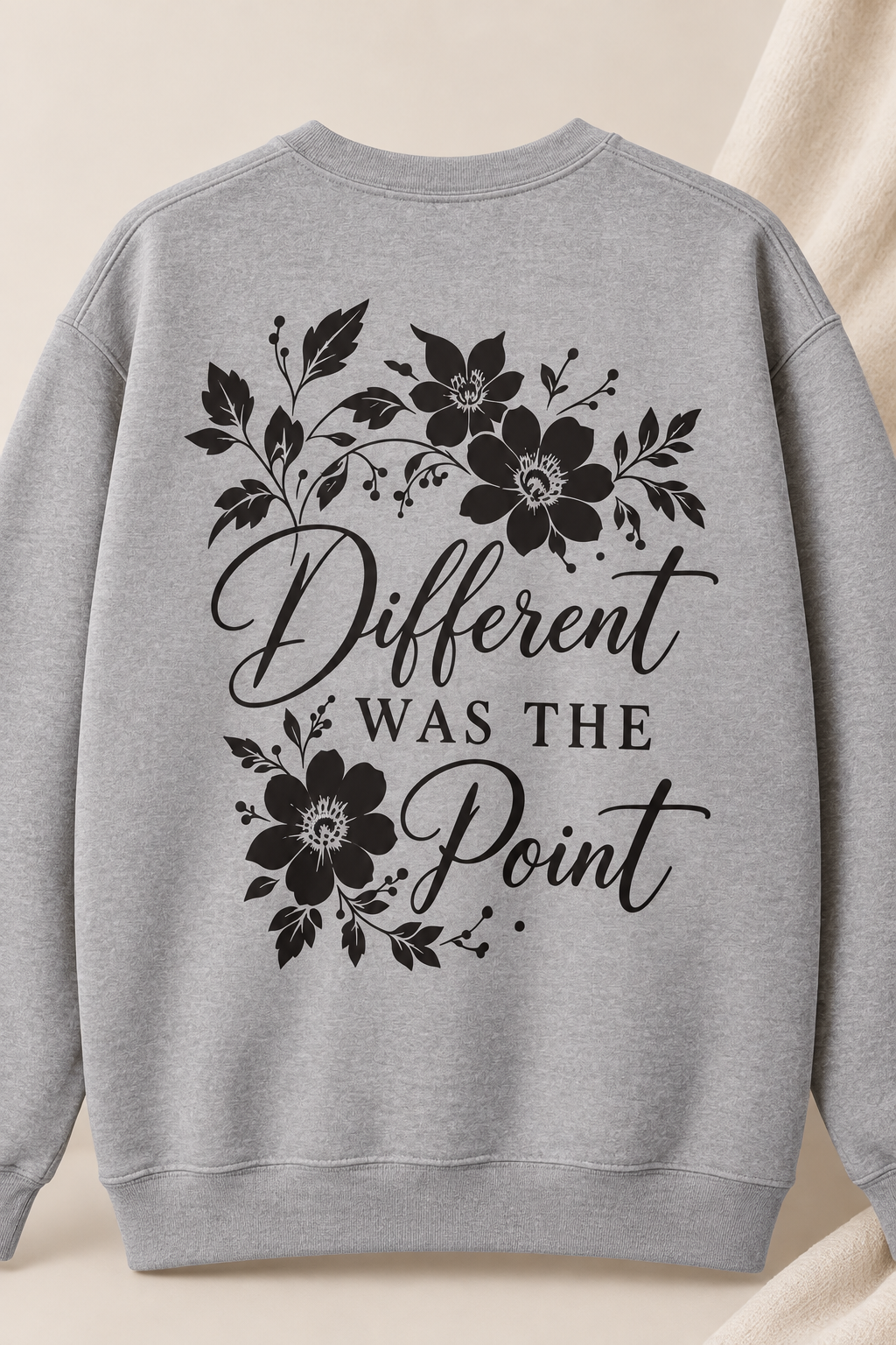 A light heather gray crewneck sweatshirt featuring a black graphic print on the front with floral illustrations and the text 'Different WAS THE Point' in a mix of script and serif fonts, displayed against a soft beige background.