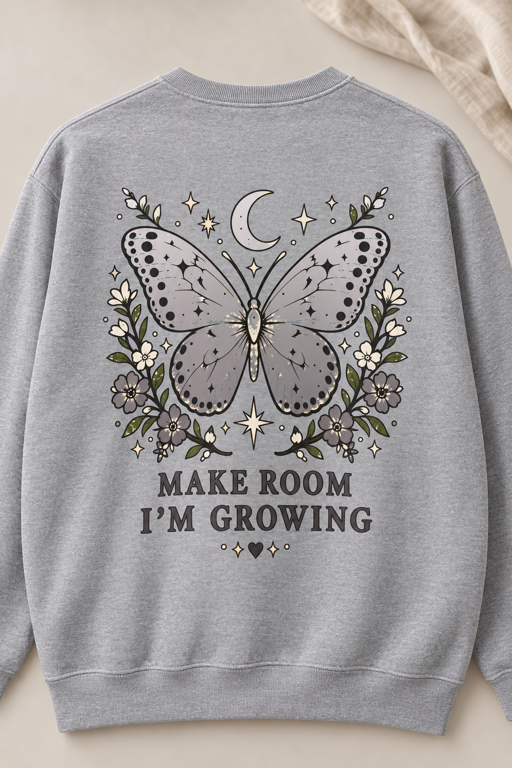 A light gray crewneck sweatshirt featuring a detailed graphic on the back with a butterfly, crescent moon, stars, and flowers, with the text 'MAKE ROOM I'M GROWING' printed below.