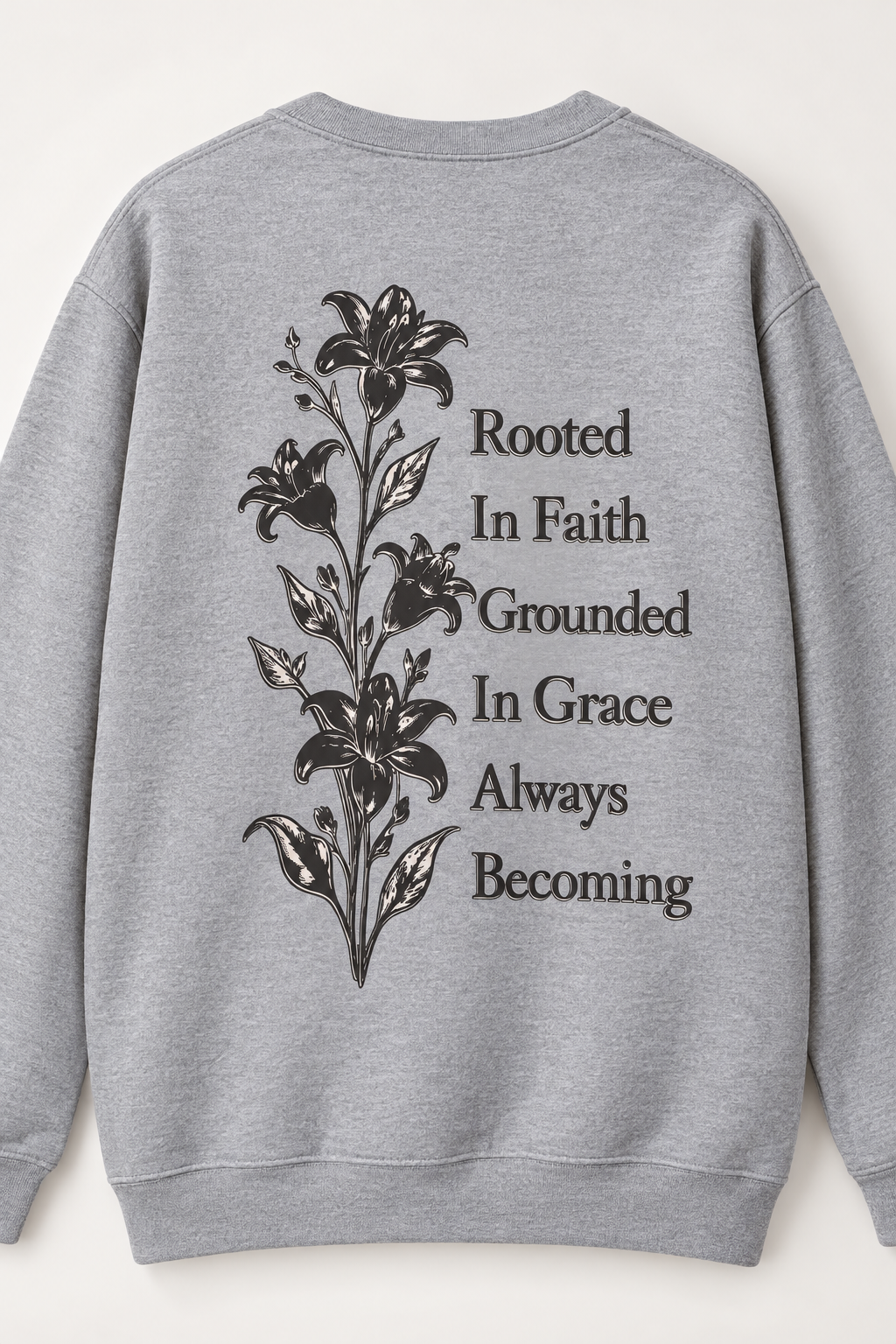 A heather gray crewneck sweatshirt shown from the back, featuring a black floral lily graphic and the inspirational text 'Rooted In Faith Grounded In Grace Always Becoming'.