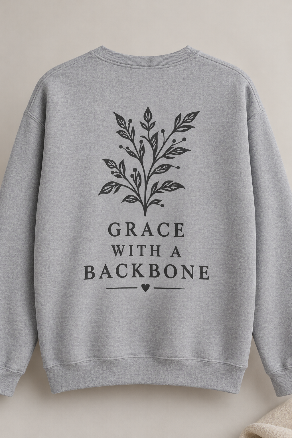 A light heather gray crewneck sweatshirt shown from the back, featuring a dark gray botanical branch graphic above the text 'GRACE WITH A BACKBONE' and a small heart.