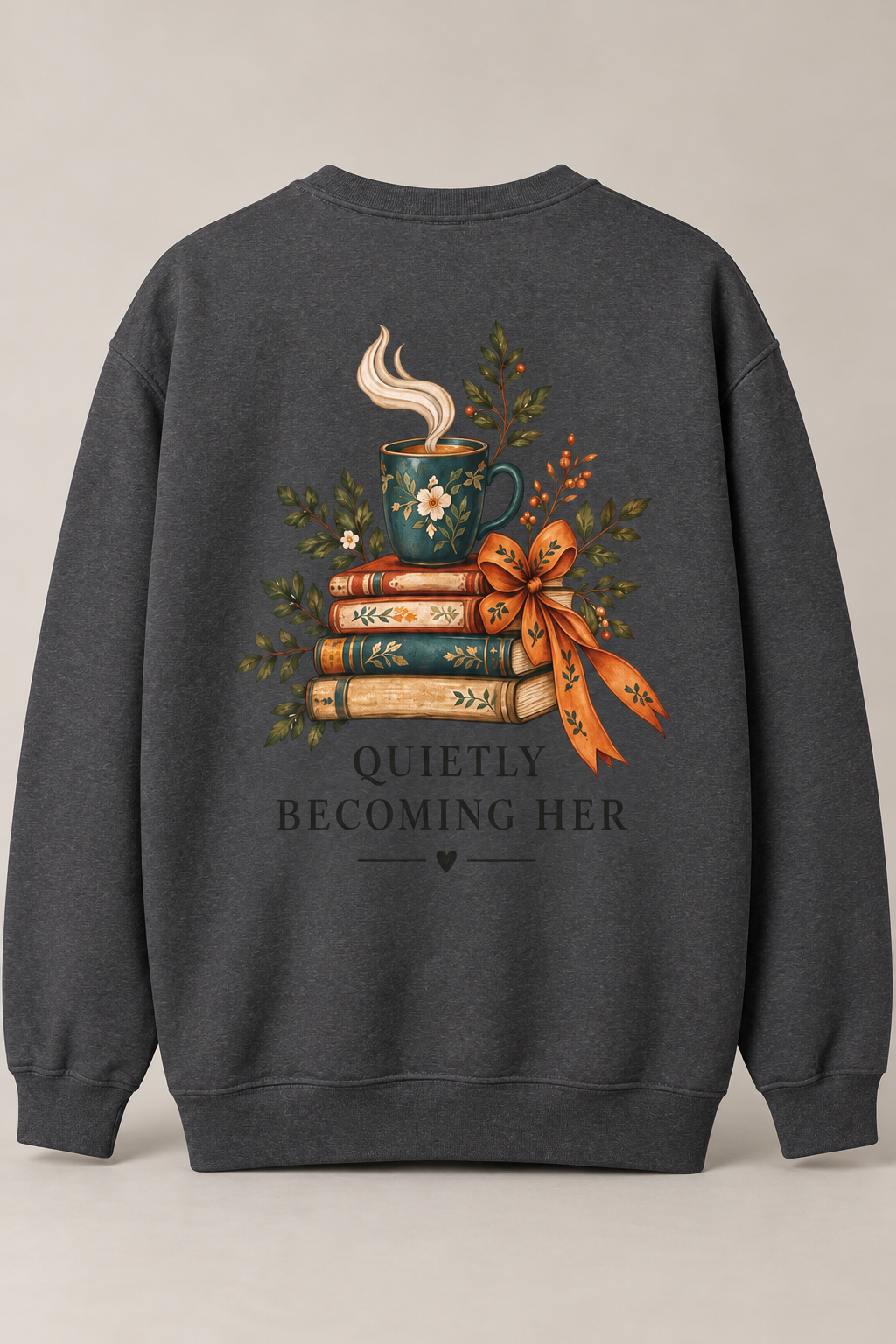 A dark heather gray crewneck sweatshirt shown from the back, featuring a detailed graphic of a steaming teal mug on a stack of books with a bow, surrounded by greenery, and the text 'QUIETLY BECOMING HER'.